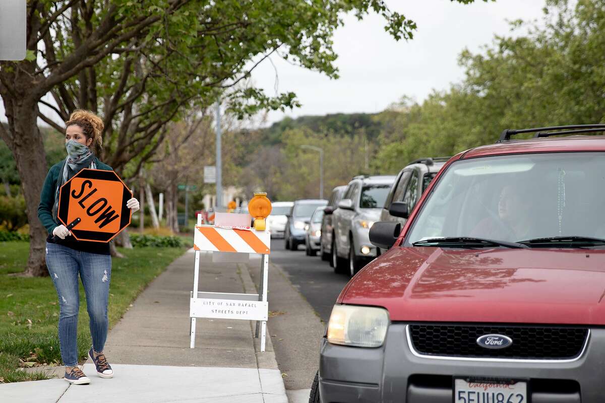 A woman directs traffic and instructs visitors to open their trunks before driving through a food bank pick-up at the San Francisco-Marin Food Bank in San Rafael, Calif. Saturday, April 11, 2020. San Francisco-Marin Food Bank has set up several new distribution centers, including this drive-through one in San Rafael where residents pull up, pop their trunks and have the goods dropped in.