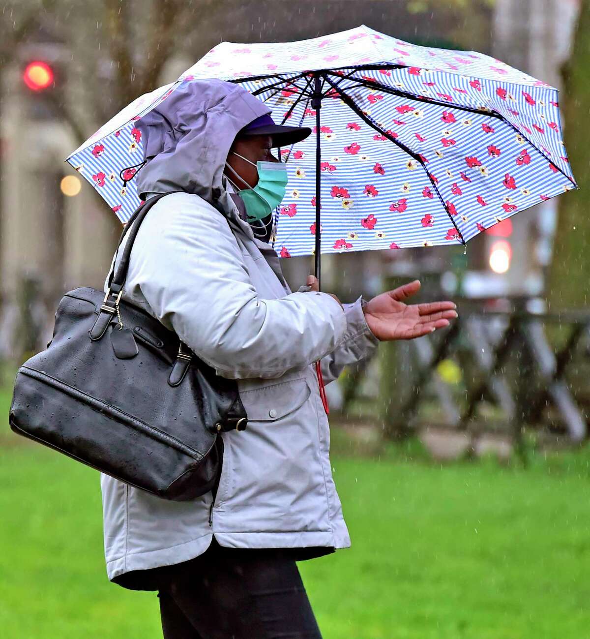 A woman wearing a face mask because of the coronavirus pandemic traverses the New Haven Green Monday in the rain.