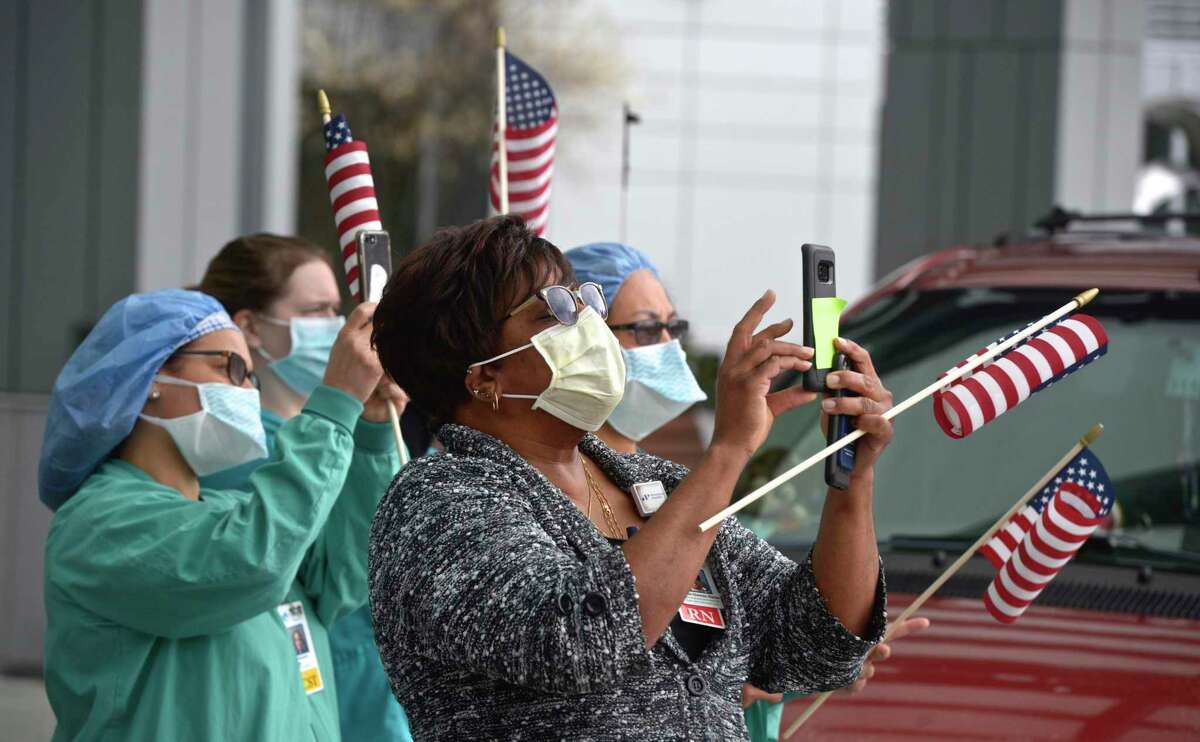 Orleen Dawes-Slater, center, and other Danbury Hospital employees photograph a 50 foot American flag that was set up at the hospital by Kyle DeLucia, owner of K&J Tree Service and his crew on a crane. They wanted to show their appreciation to the hospital staff serving the community during the covid pandemic. Tuesday, April 14, 2020, in Danbury, Conn.