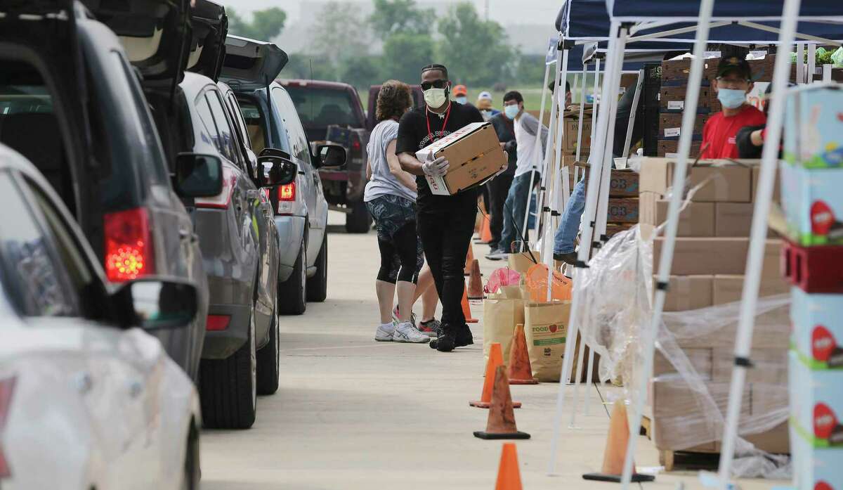 Helpers load food into cars as people in cars gather at Traders Village to get food from the San Antonio Food Bank on Thursday, April 9, 2020. The coronavirus pandemic has put enormous strain on households and their food budgets across the city. (Kin Man Hui/The San Antonio Express-News via AP)