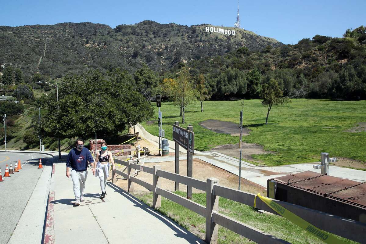 Two people wearing protective face masks are seen walking with a view of the Hollywood Sign in the background on April 14, 2020 in Los Angeles, California. Worldwide, the coronavirus (COVID-19) pandemic has claimed over 120,000 lives and infected over 1.9 million people.California.