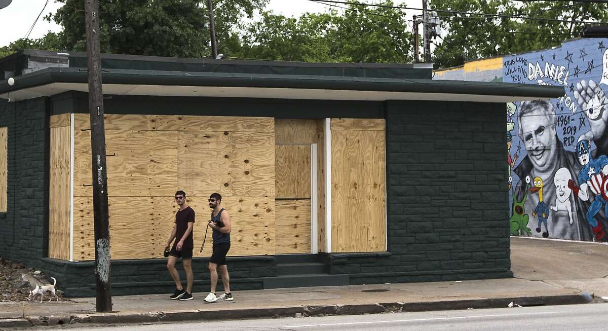 People walk past a boarded up business on Westheimer in the Montrose area on Saturday, March 28, 2020 in Houston. Businesses around the city have been closed and boarded up due to the coronavirus pandemic precautions, forcing several businesses to shut their doors.