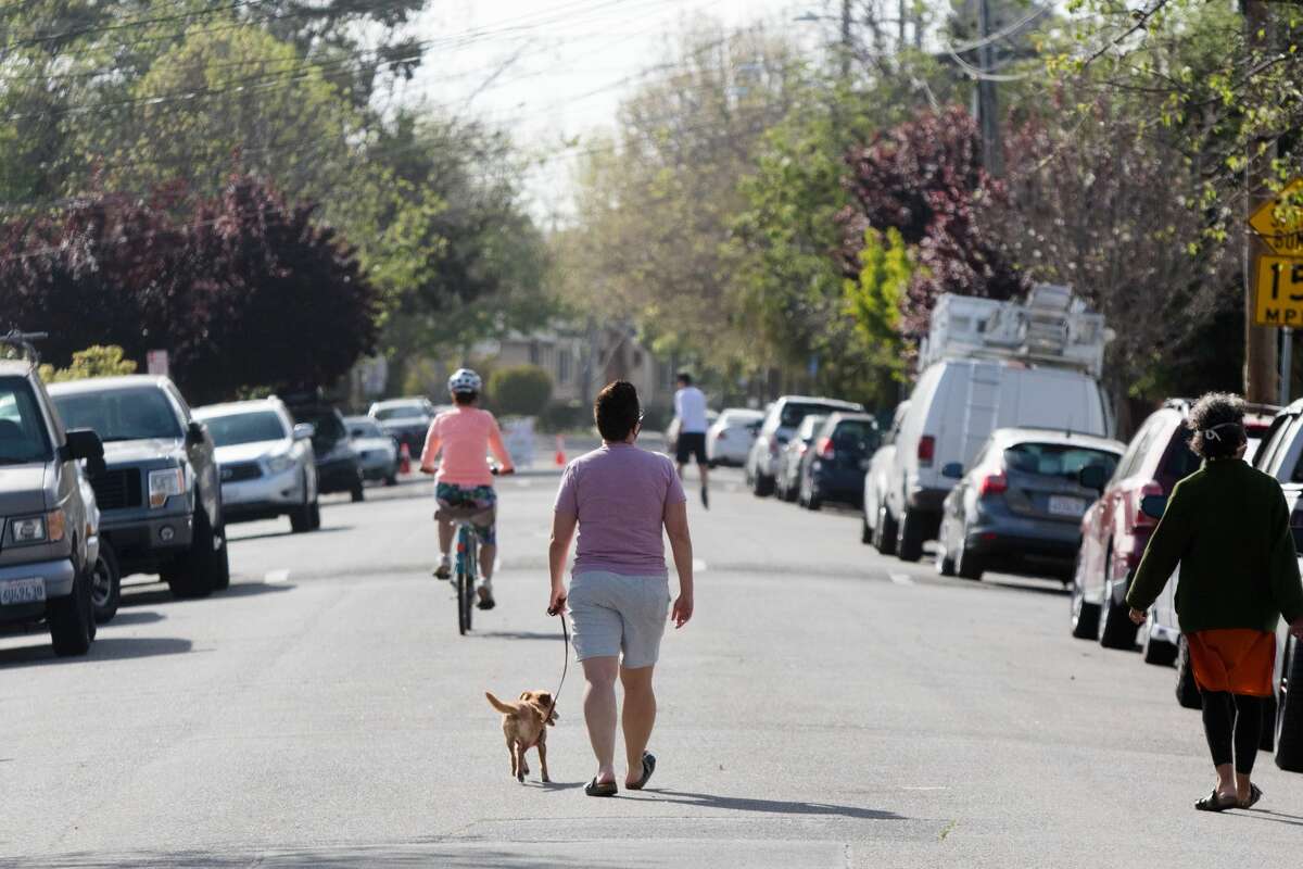 People walk and ride bikes down 42nd Street in Oakland, Calif. on April 15, 2020. The city's "slow street" program started with four streets, where signs, barricades and cones were placed to signify the soft closure of the street for pedestrian and to encourage physical activity.
