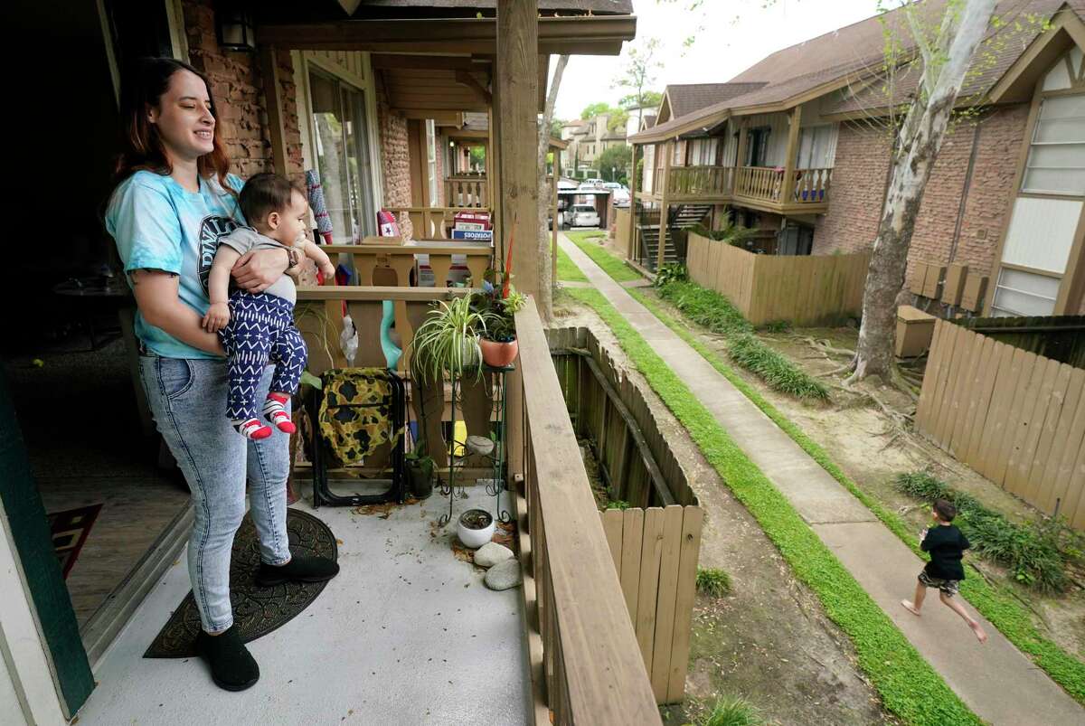 Ruthy Raske holds her 8-month-old son, Santi, as she watches her other son, J.P., 7, play on the sidewalk in front of their Memorial area apartment Wednesday, March 18, 2020, in Houston. She is a server at a restaurant that just had to close its dining room for two weeks. She's about to move into a larger unit at her complex and is worried about her job and paying rent.