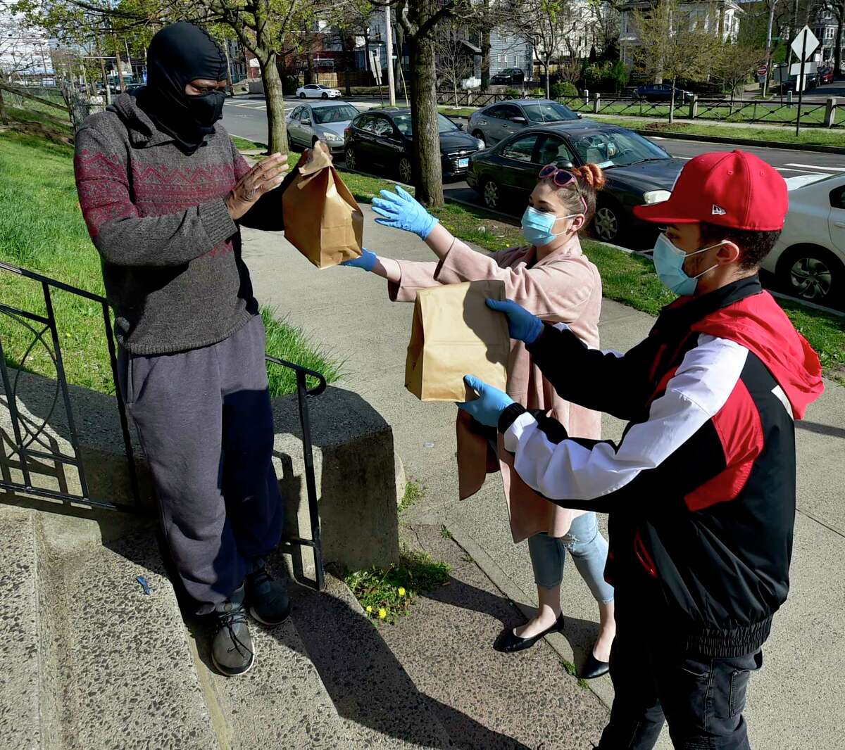 New Haven, Connecticut - Thursday, April 16, 2020: Xanthia Pellegrino, 27, of Branford, center, who grew up poor in New Haven, delivers food on Chapel Street with her boyfriend Darren Bowman, Jr. of Hamden, 25, right, to Christopher Staggers of New Haven. Pelligrino has been laid off from her job so she is cooking meals for families with children, elderly, people with medical issues and basically anyone who needs her home cooking during the Coronavirus / Covid-19 pandemic. Staggers, on disability and needs dialysis, says the her foods helps him with his diabetic diet.