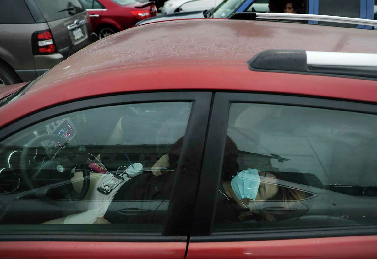 Mariah Garza sleeps in her car with Ryan Torres while waiting for the emergency food distribution to begin Friday, April 17, 2020, at the Alamodome. They arrived at 6 a.m.