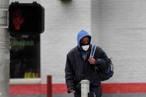 A man wears a protective mask as he waits to cross a street.
