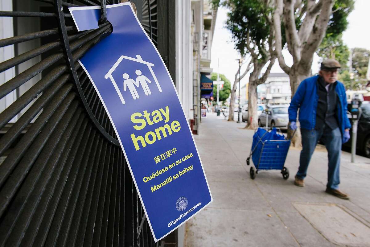 Pedestrians pass by a social distancing sign on a residential gate put up by San Francisco's Latino Task Force on COVID-19 members, in San Francisco, Calif, on Friday, April 17, 2020.