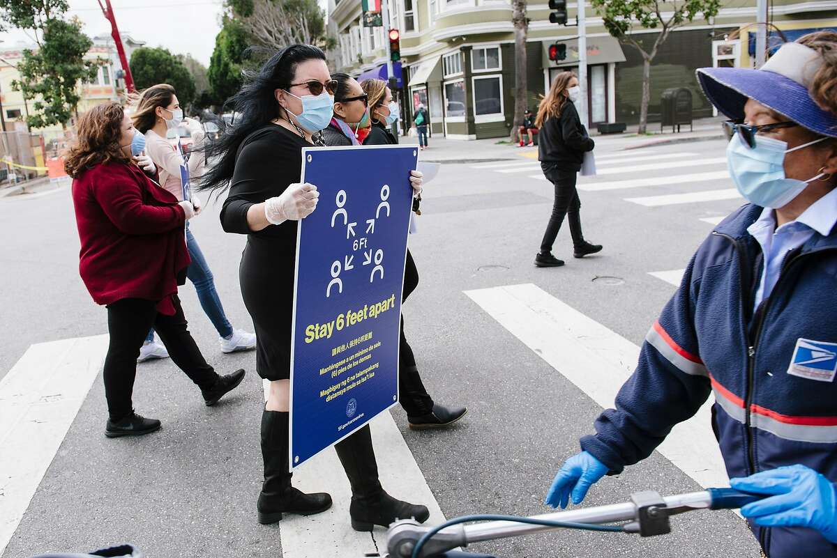 San Francisco Latino Task Force on COVID-19 member Valerie Tulier-Laiwa, holds a social distancing poster as her group crosses 24th Street while putting up signs, in San Francisco, Calif, on Friday, April 17, 2020.