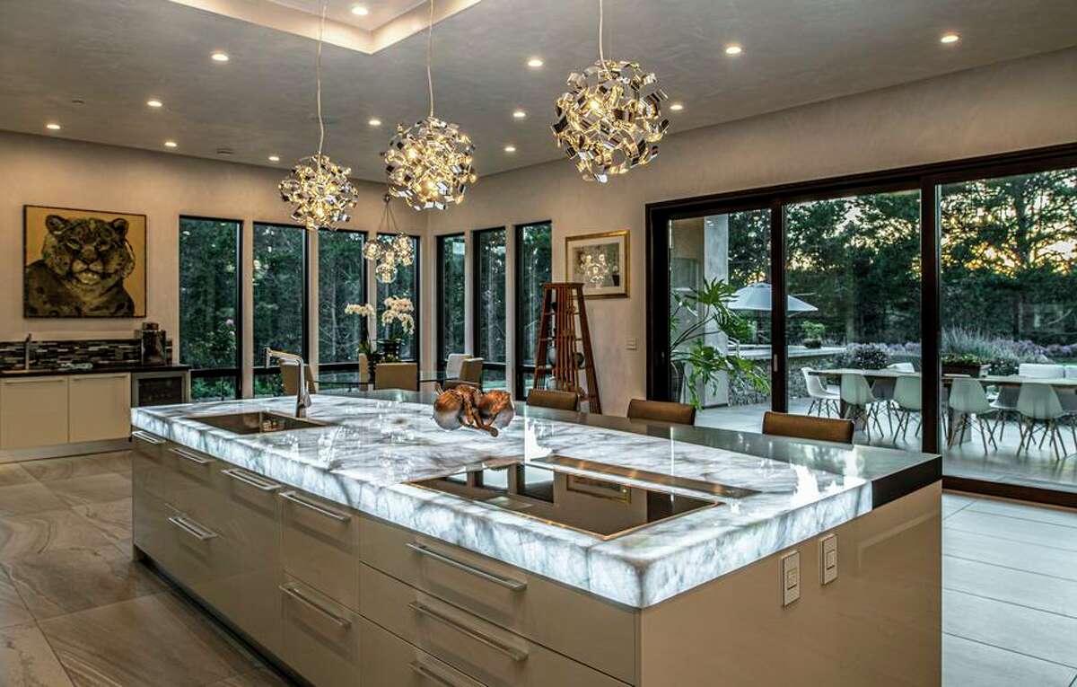 Modern pendant lights illuminate the kitchen’s stone-topped island that features an induction cooktop.