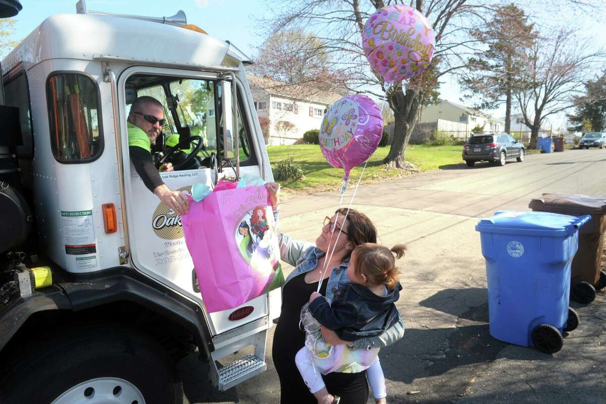 Truck drive Vinnie Yulo for Oak Ridge Waste and Recycling hands a bag of presents and balloons to birthday girl Isabella Stevens and her mother Ashley in front of their family home in Shelton on Friday. Oak Ridge Waste and Recycling delivered presents and balloons to Isabella as a surprise on her 2nd birthday Friday.