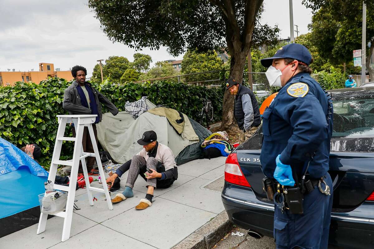 A police officer asks a group of homeless men to social distance themselves from one another outside a tent encampment on Oak Street on Sunday, April 19, 2020 in San Francisco, California.