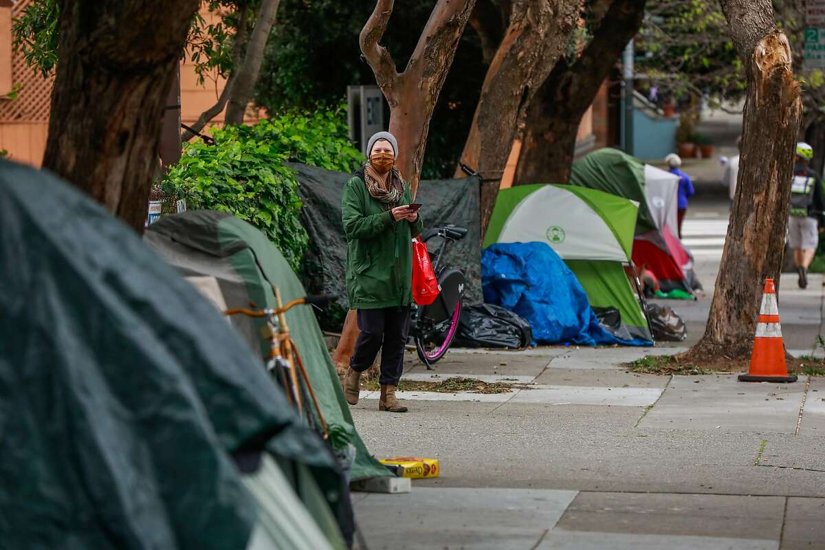 A pedestrian passes by a tent encampment on Broderick Street on Sunday, April 19, 2020 in San Francisco, California.