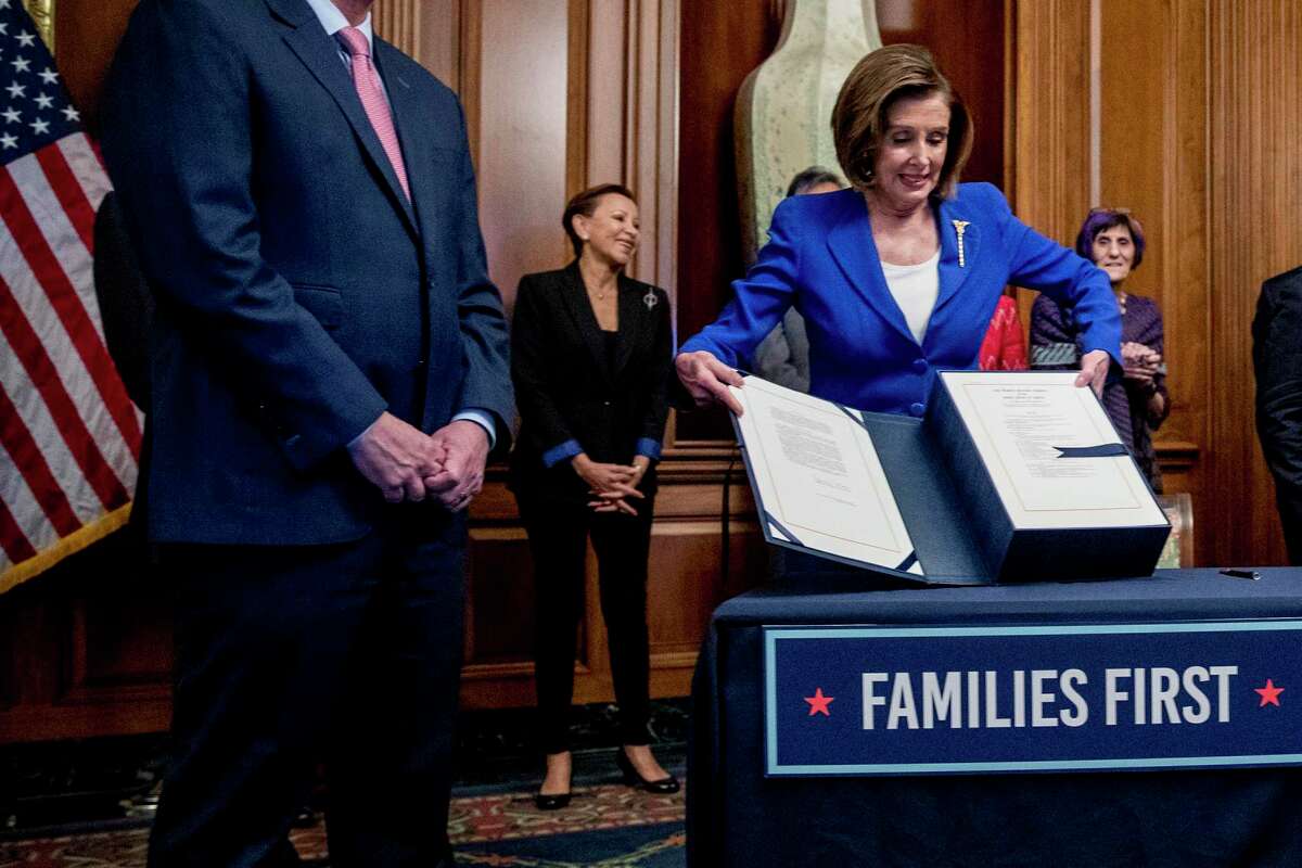 House Speaker Nancy Pelosi, right, lifts the Coronavirus Aid, Relief, and Economic Security Act after signing it on Capitol Hill March 27 in Washington, D.C.