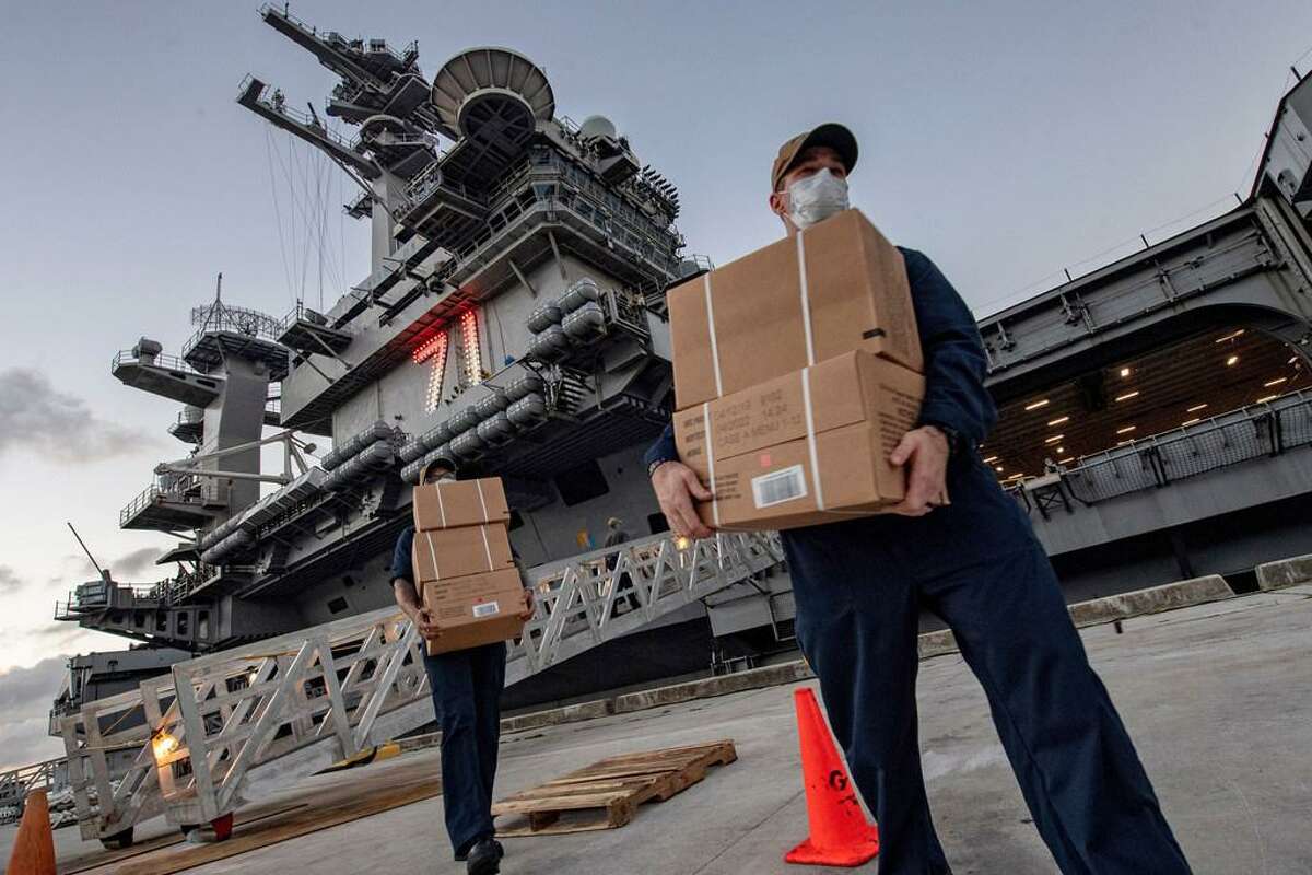 In this April 7, 2020, photo released by the U.S. Navy, sailors assigned to the aircraft carrier USS Theodore Roosevelt move ready to eat meals for sailors who have tested negative for COVID-19 and are being taken to local hotels in an effort to implement social distancing at Naval Base Guam.