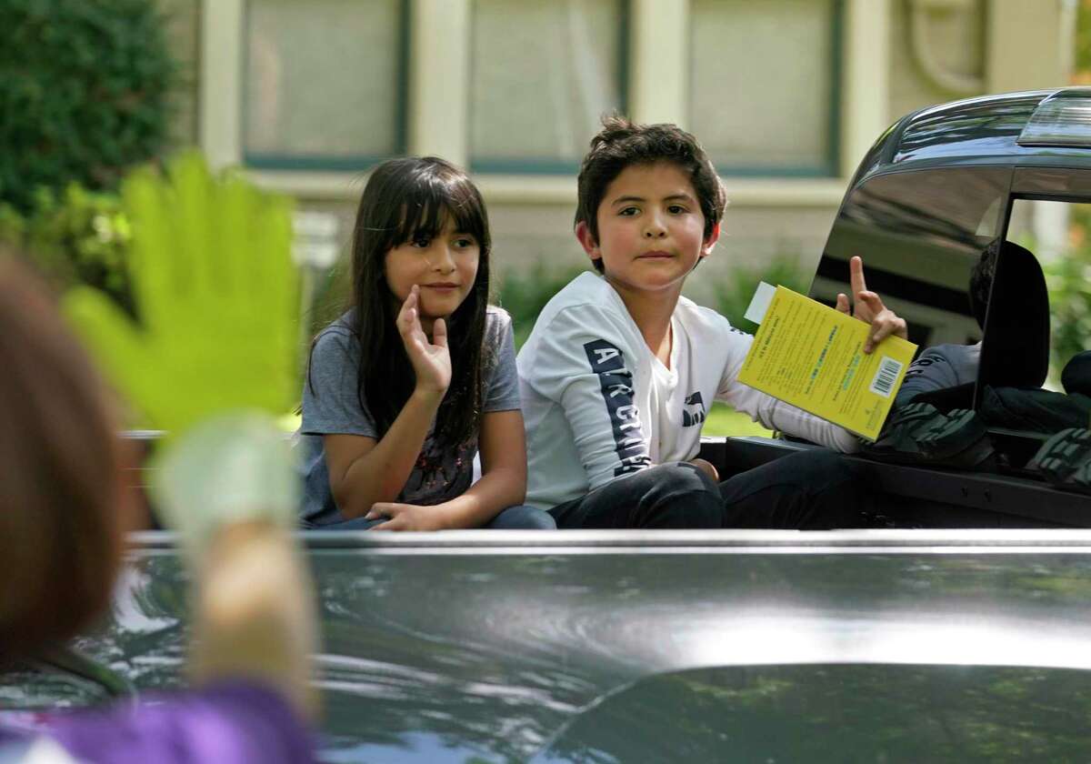 Camila Rios, a second grader, left, and her brother, Niko Rios, a fifth grader, wave after picking up their books for the One Book, One School shared reading event Thursday at Houston ISD’s Travis Elementary School. Students in HISD might return to school earlier in August or see a longer class day in 2020-21 to make up for lost instructional time due to the novel coronavirus pandemic.