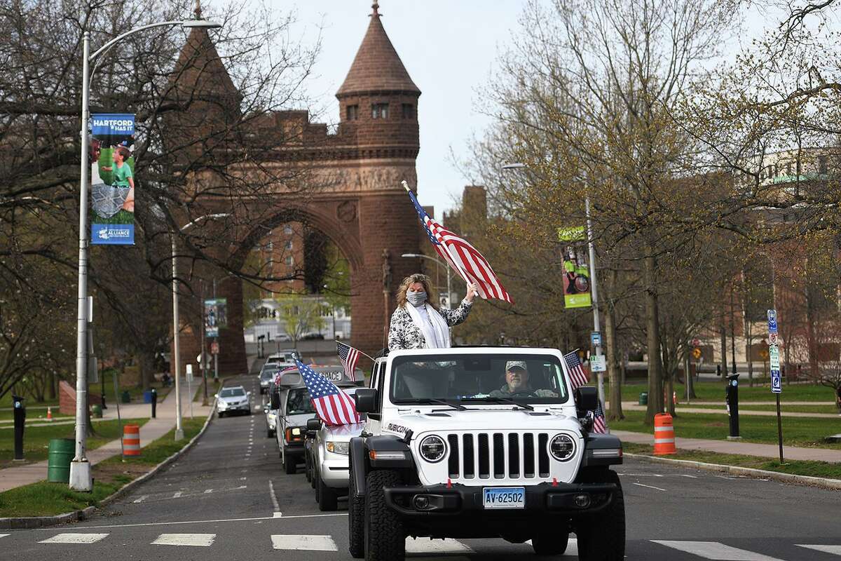 Protestors wave flags and honk horns as they parade around downtown Hartford during an “open up the state” rally on Monday.