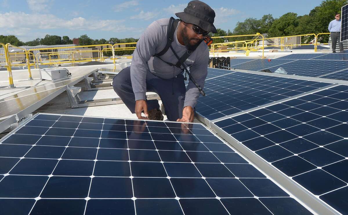 ENCON employee Andrew Richards installs solar panels on the roof of the Paul Miller Nissan dealership in Fairfield, which has installed the solar-energy array with financing from Darien-based Greenworks Lending, Wednesday, July 18, 2018, in Fairfield, Conn.