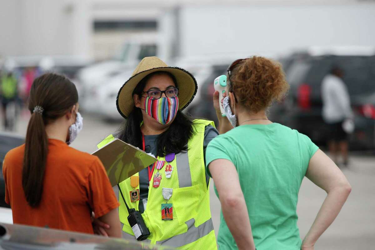 San Antonio Food Bank Director of Volunteer Services Mendy Escamilla, 44, center, checks the body temperature of volunteers for the mega food distribution at Hardin Athletic Complex, Tuesday, April 21, 2020. They were expecting 200 volunteers for each of the two shifts at the event.