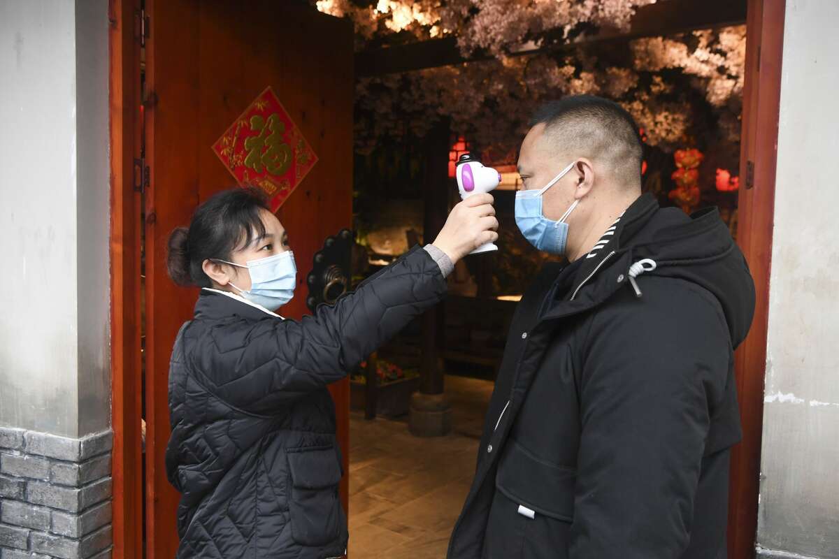 Temperature checks are also required for employees at restaurants. Shown: A staff member of a hot-pot restaurant undergoes a temperature check in southwest China's Chongqing Municipality on Feb. 15, 2020.