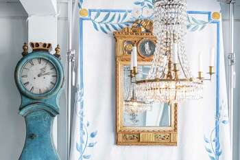 A display at Dawn Hill Antiques in New Preston features a painted panel depicting wall paintings typically found in 18th century Swedish rooms, a Gustavian period Swedish mirror, a Swedish blue painted Mora clock, and a Swedish chandelier; the two chairs are a pair of Swedish Lindome dining chairs, circa 1790.