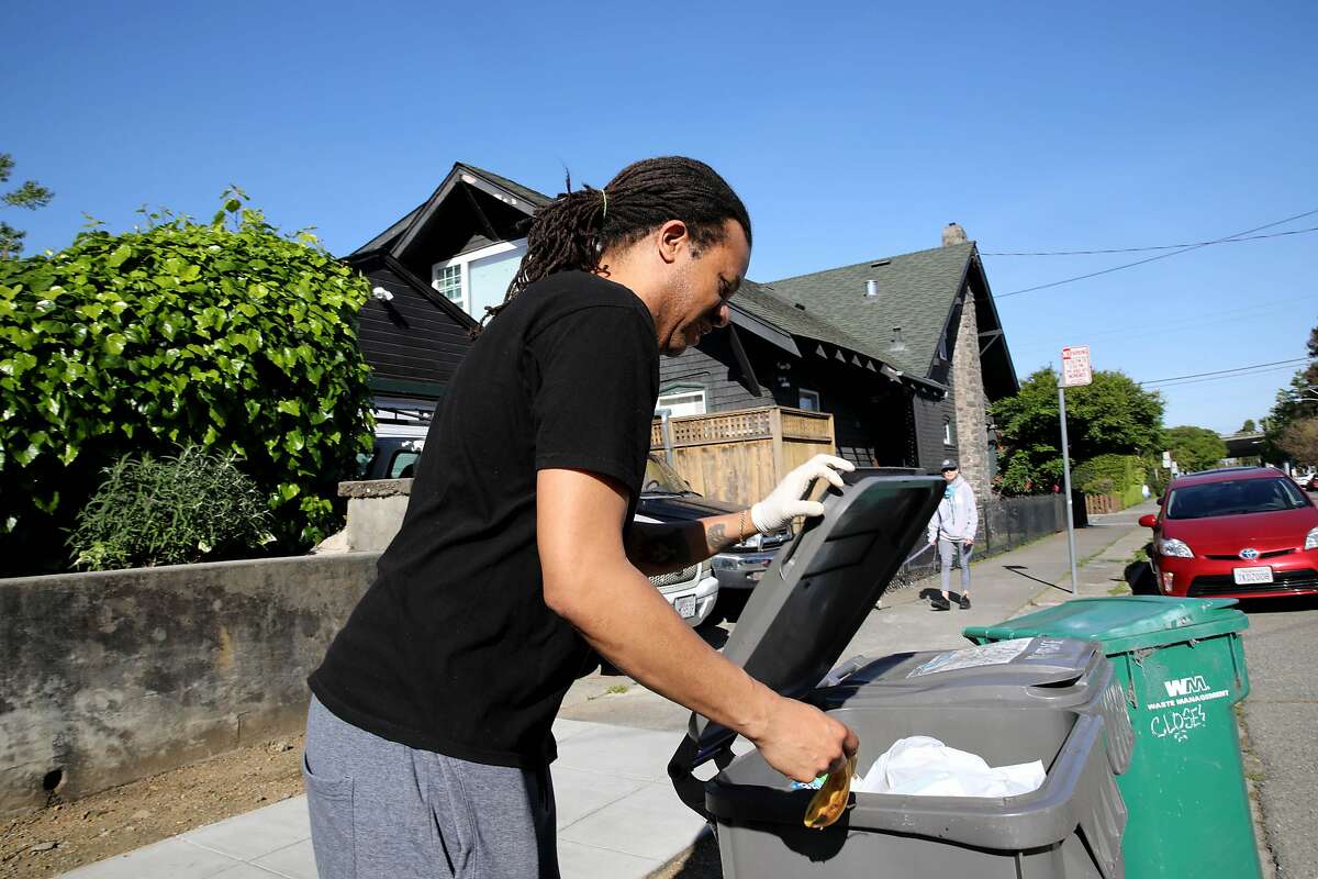 Chronicle columnist Otis Taylor places a juice carton into a recycles bin as he awaits Alvin Aragon, 50, to collect his recyclables in the Rockridge neighborhood on Wednesday, April 22, 2020, in Oakland, Calif. Aragon drives a truck for California Waste Solutions, which handles Oakland's recycling contract. Aragon, who was raised in Oakland and is now raising his family in the city, says he touches about 1,000 containers a day. Sanitation and recycling loads have increased since we were told to stay inside. We're told to watch what we touch, but workers like Aragon put their hands on the containers filled with stuff we've discarded. We touch everything," he said. Aragon's worried about getting his family sick. He wears plastic gloves under his work gloves. He washes off before leaving work and then takes a shower when he gets home.