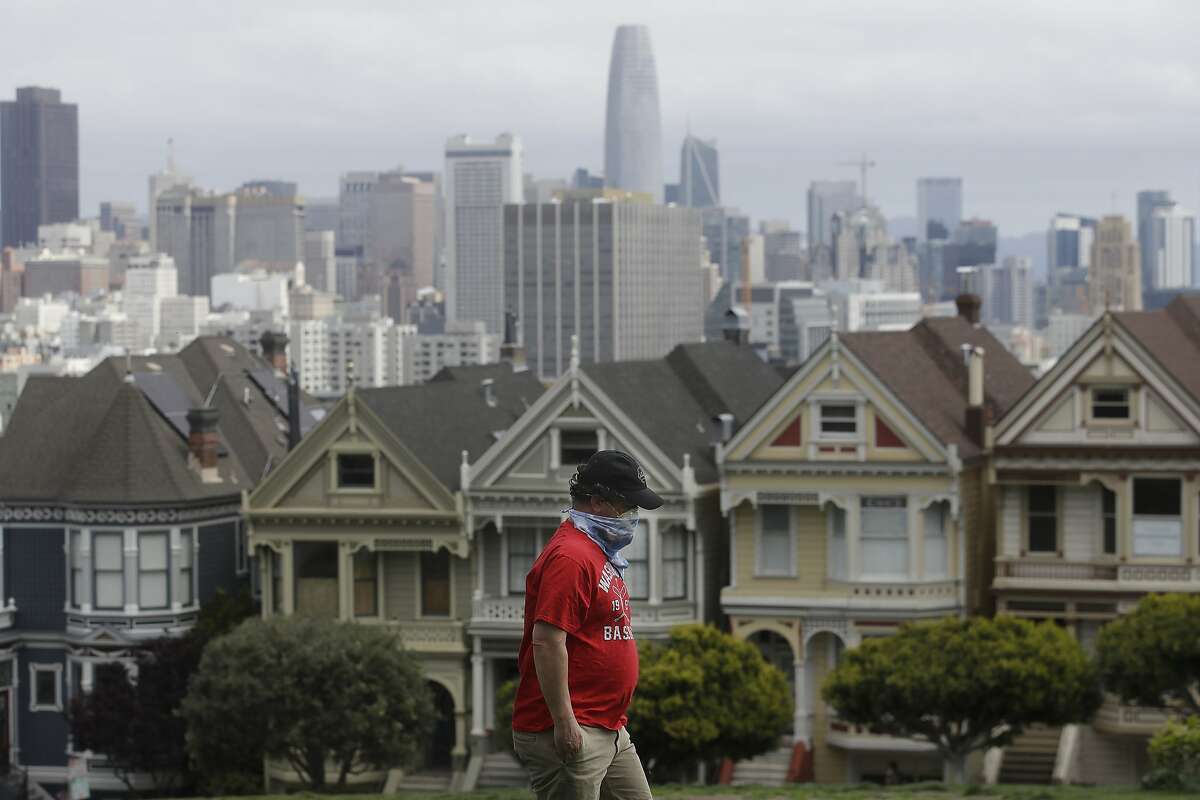 A man wearing a mask walks in Alamo Square Park in front of the "Painted Ladies," a row of historical Victorian homes, in San Francisco, Sunday, April 19, 2020, during the coronavirus outbreak. (AP Photo/Jeff Chiu)