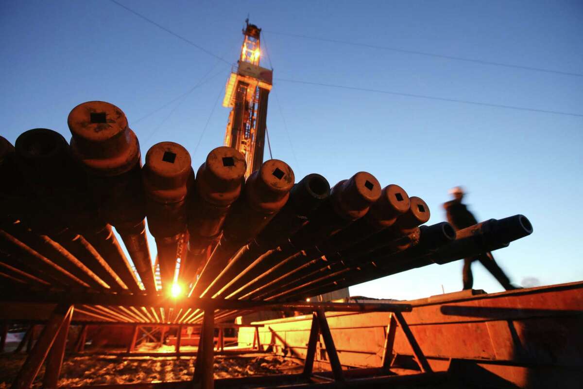 A worker passes an illuminated oil drilling rig and drill pipes, operated by Rosneft, near Nizhnevartovsk, Russia, on March 21, 2017.