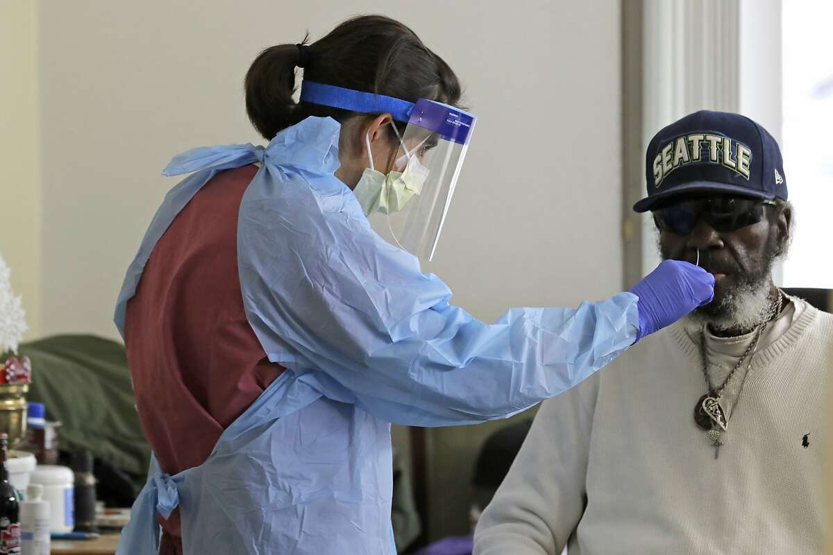 In this April 17, 2020, photo, Dr. Gabrielle Beger, left, takes a nose-swab sample from Lawrence McGee, right, as she works with a team of University of Washington medical providers conducting testing for the new coronavirus at Queen Anne Healthcare, a skilled nursing and rehabilitation facility in Seattle. More than 100 residents were tested during the visit, and the results for all were negative, according to officials. Sending "drop teams" from University of Washington Medicine to conduct universal testing at skilled nursing facilities in collaboration with public health officials is one aspect of the region's approach to controlling the spread of the coronavirus. (AP Photo/Ted S. Warren)
