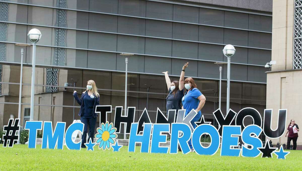 A trio of workers in the Texas Medical Center pose for a photo by a sign thanking the “TMC Heroes” working to fight the coronavirus pandemic on Tuesday, April 7, 2020 in Houston.