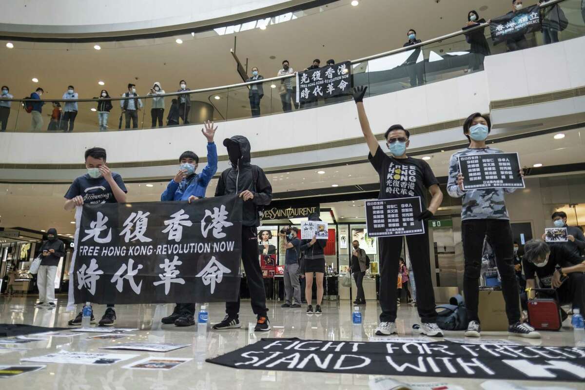 Demonstrators wearing protective masks hold placards and banners while standing spaced apart during a protest in the atrium of the International Finance Center Mall in Hong Kong on April 24, 2020.