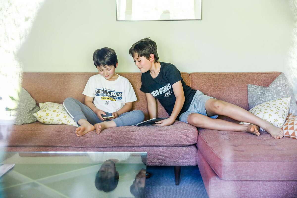 (L-r) Hugo Jermyn, 5 shows something to his brother Aalto Jermyn ,10 while reading on devices at their home during shelter-in-place orders on Thursday, April 23, 2020 in Berkeley, California.