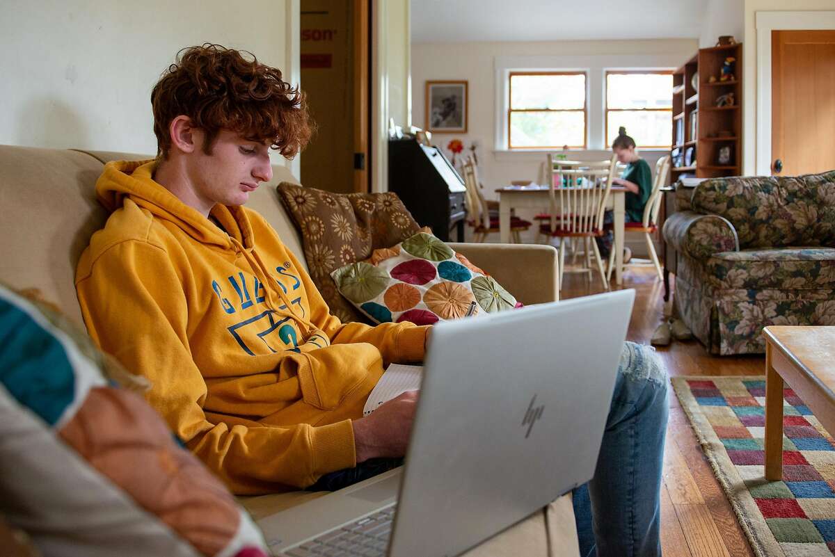 Jasper Schoenberger (18) an Oakland Tech high school senior, does homework at home with his sister Juliette, (11) while they self isolate during the shelter-in-place order on March 20,2020 in Oakland, Calif.
