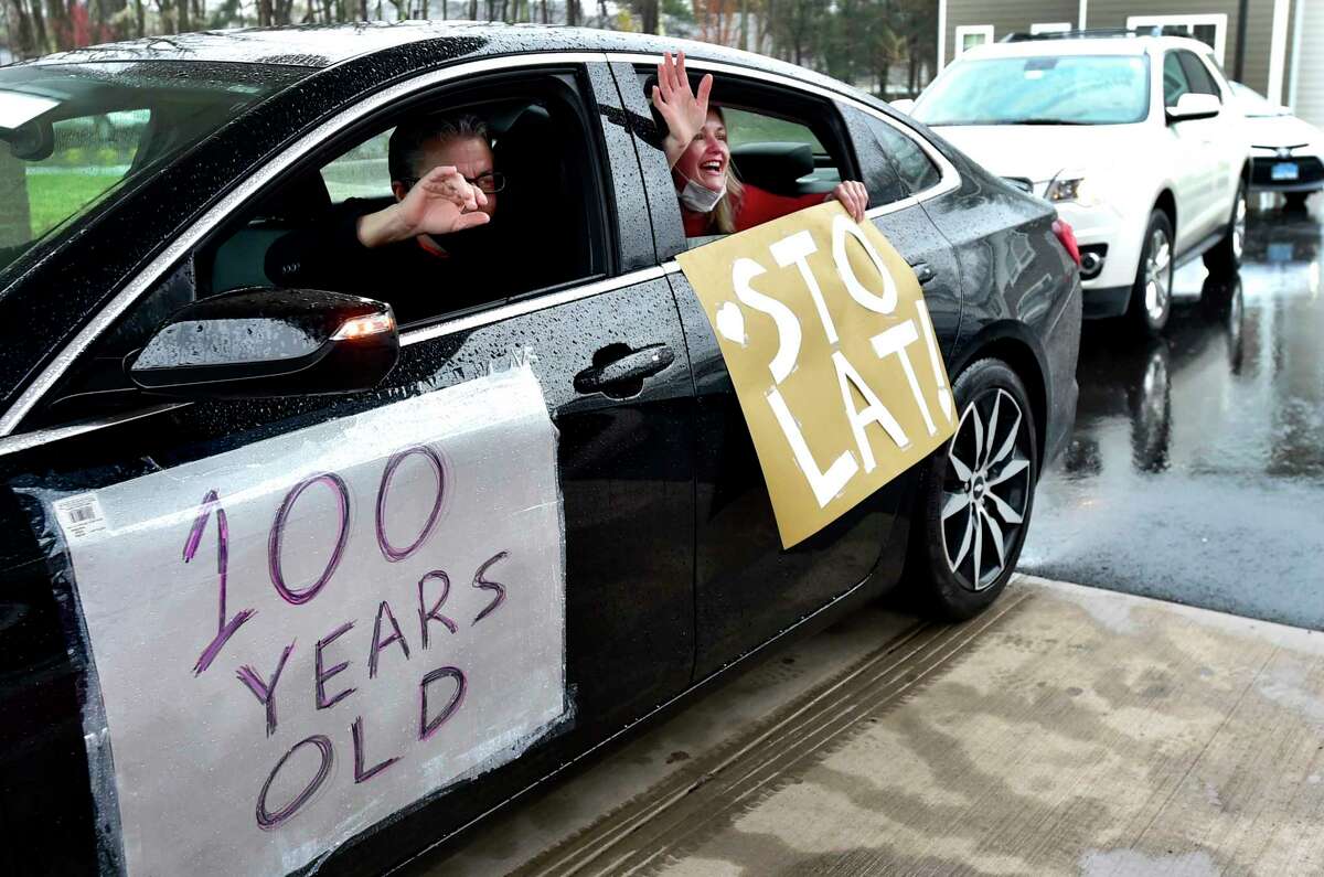 North Haven, Connecticut - Friday, April 24, 2020: Cathy DellaValle of Haven, right, holds a sign "Sto lat", the name of a Polish song that is sung to express good wishes, good health and long life to a person during a celebratory procession Friday honoring her father Edward Otremba Sr., 100, a resident at The Landing of North Haven assisted living facility, during his centennial birthday party using social distancing with a community car parade that included a North Haven Fire Department truck, the presentation of a birthday cake, and birthday songs in English and Polish. Ed?•s family was planning on a huge celebration at the community with friends and family but it had to canceled because of the Coronavirus / Covid-19 pandemic