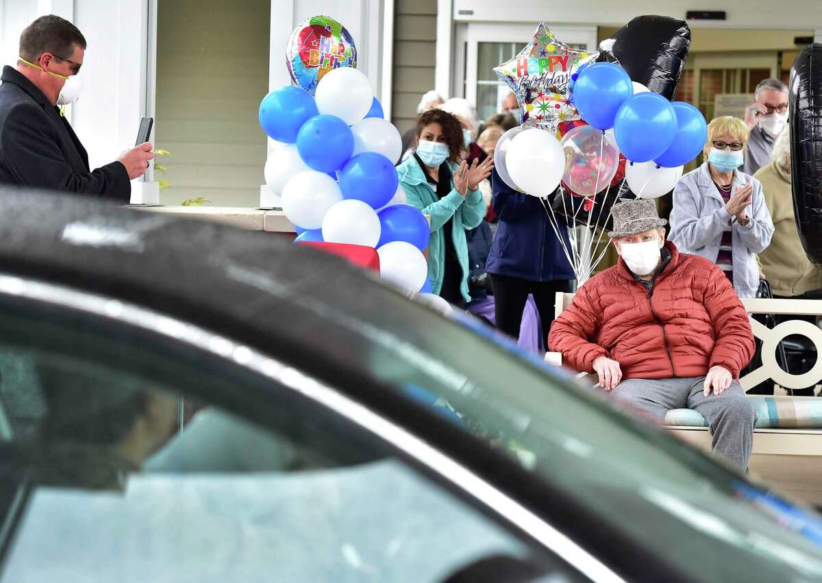 Edward Otremba Sr., a resident at The Landing of North Haven assisted living facility, seated, left, gets a 100th birthday celebrationFriday using social distancing with a community car parade that included a North Haven Fire Department truck, the presentation of a birthday cake, and birthday songs in English and Polish.