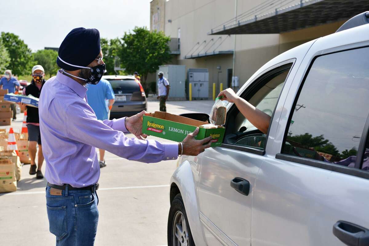 Vikram Singh of the Sikh Dharamsal of San Antonio offers peanut and jelly sandwiches to a family in line Saturday during a food distribution at the San Antonio Food Bank.