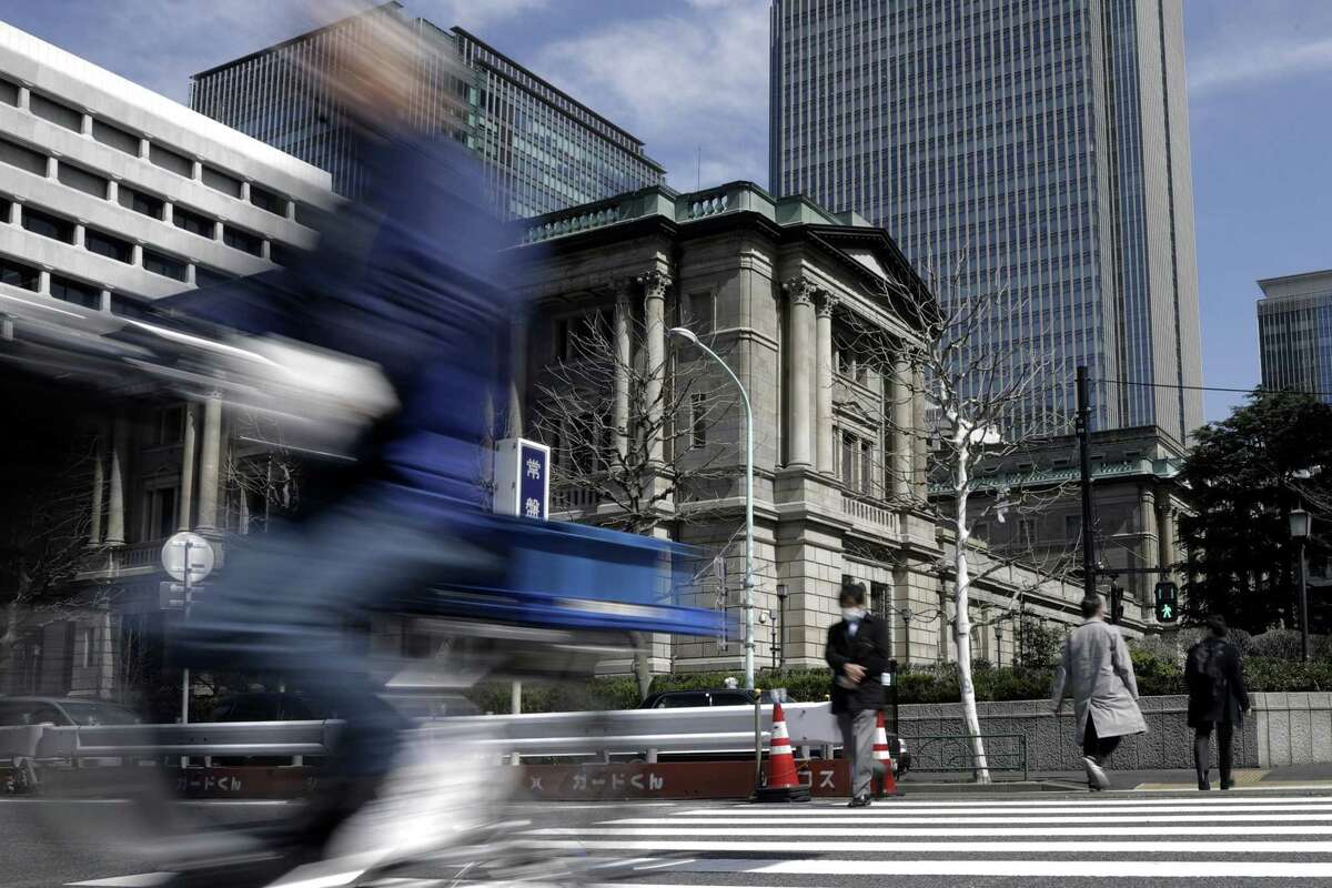 Pedestrians cross a road in front of the Bank of Japan headquarters in Tokyo on March 16, 2020.