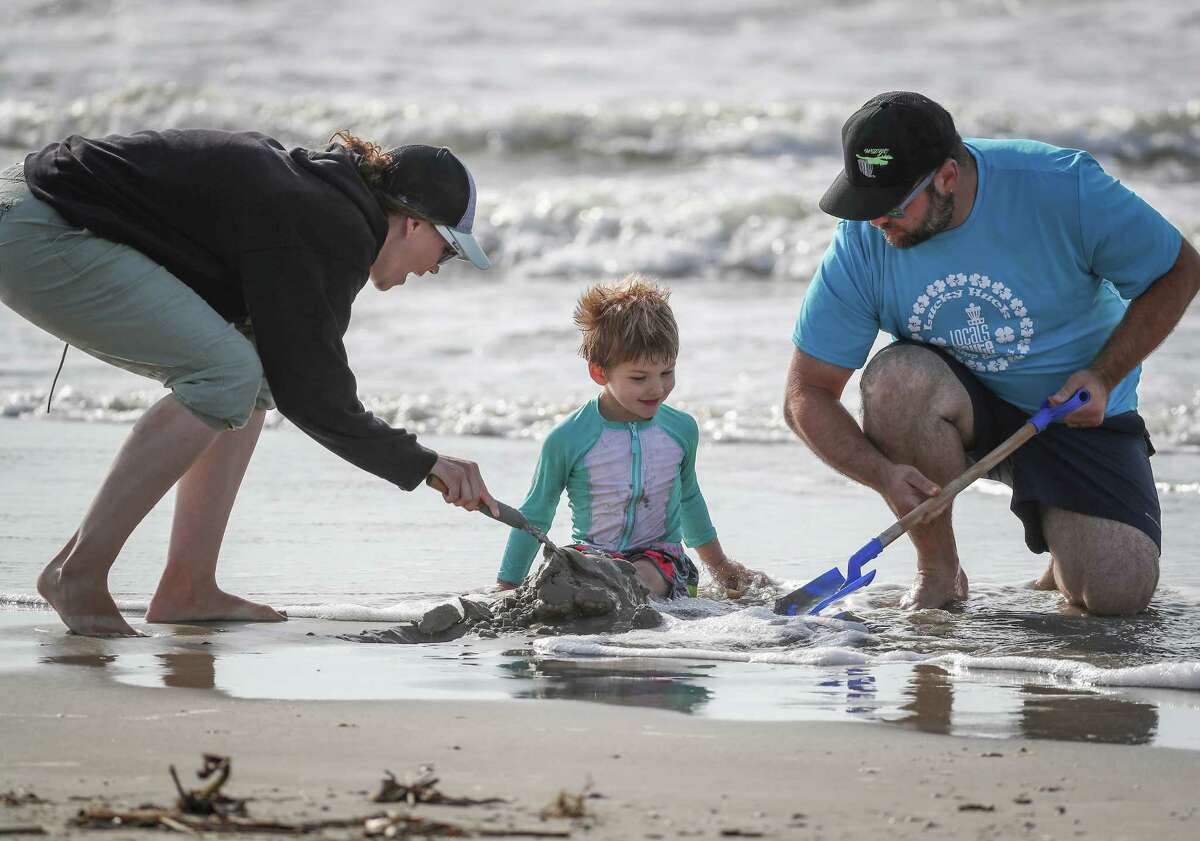 Madison (left) and Jesse Tomaino (right) cover their son's, Miles, 3, legs with sand after the city of Galveston partially reopened public beaches after closing them for nearly a month due to the novel coronavirus outbreak Monday, April 27, 2020, in Galveston. The Tomaino family are from Oregon decided to shelter in place in Galveston instead of driving across the United States to return home.