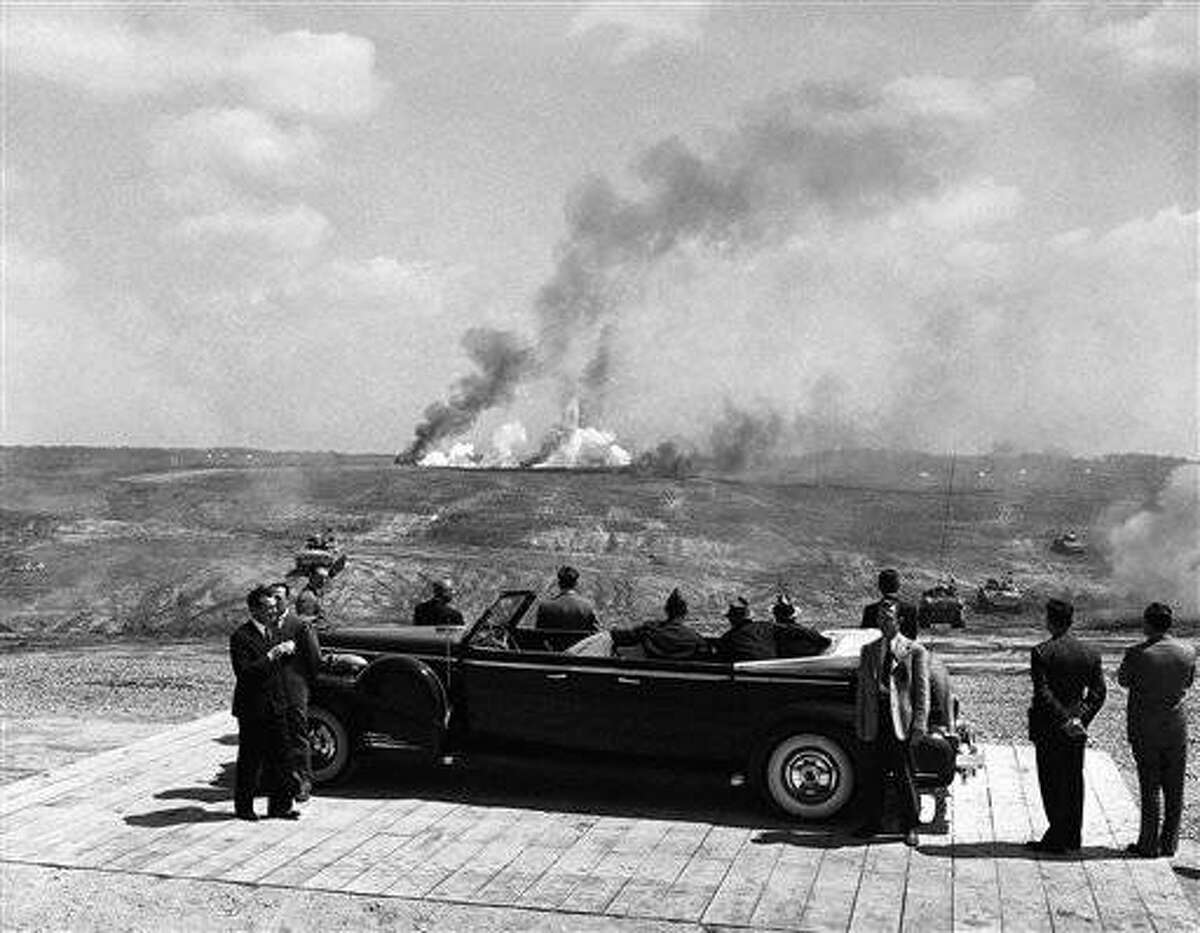 Thunder from exploding live ammunition lend realism to the practice battle staged by troops at Fort Knox, Kentucky on April 28, 1943 for U.S. President Franklin D. Roosevelt. Tanks advance at right and left with their shells bursting in far background. With the President, who is on far side of car, are Lt. Gen. Jacob L. Devers, Chief of armored forces, left, and Gov. Keen Johnson of Kentucky, center. (AP Photo)