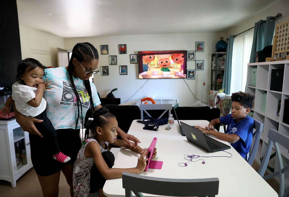 Kenya Pierce, 30, holds her 13-month-old baby Nyeri Rutherford as she helps her daughter, Nairobi Banks, 7, with her math lesson, while son Dannon Lemon, 12, works on his computer in their home on Tuesday, April 28, 2020, in Richmond, Calif. Pierce, who formally worked for WIC for nine years, is currently receiving WIC benefits.
