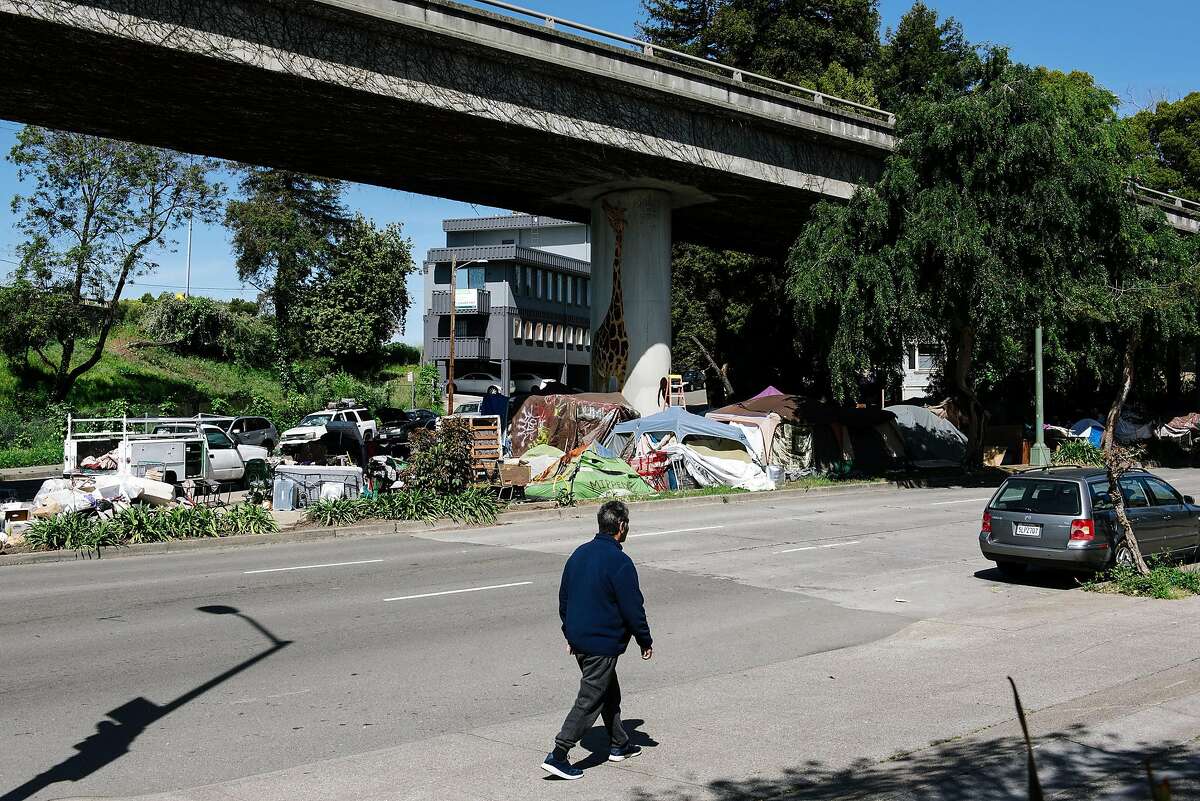 A person walks past a homeless encampment underneath Interstate 580 in Oakland, Calif, on Friday, April 22, 2020.
