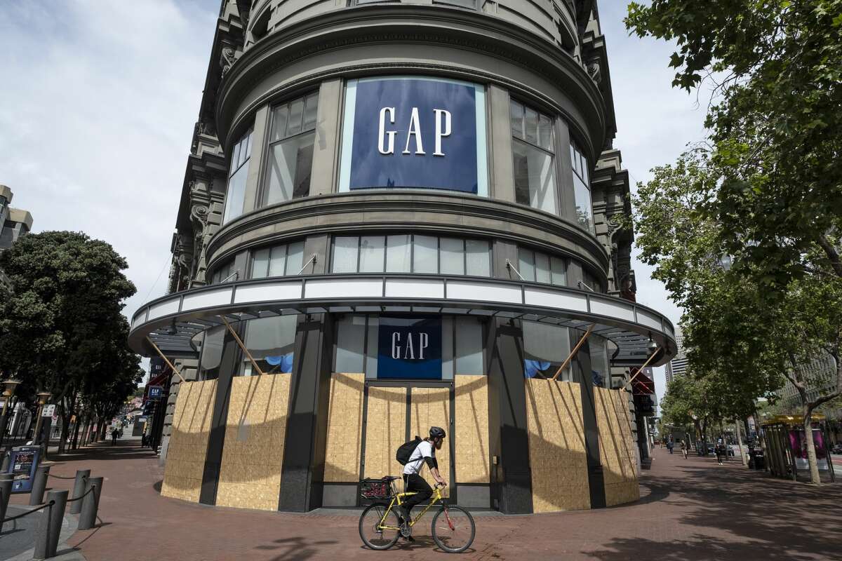 In this photo taken Friday, April 17, 2020, a man rides his bicycle past the boarded up and closed Gap store near Union Square in San Francisco.