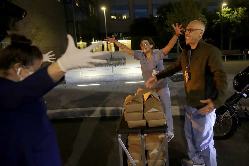 Nightbird Restaurant chef and owner Kim Alter, left, mimics giving a hug to nurse practitioner Sydney Gressel, center, and patient care technician Matt Phillips after delivering dinner to them at University of California at San Francisco Benioff Children's Hospital in San Francisco, March 27, 2020. A group of tech-savvy, entrepreneurial San Francisco friends wanted to help two groups devastated by the coronavirus pandemic. They came up with a plan that involved soliciting donations, tapping friends in the restaurant world and getting San Francisco hospitals to accept free food cooked up by some of the city's top chefs.