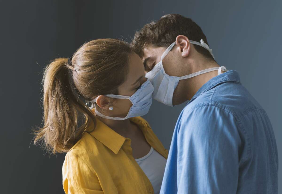 Young couple wearing protective face masks and kissing each other, virus spread prevention and people concept.