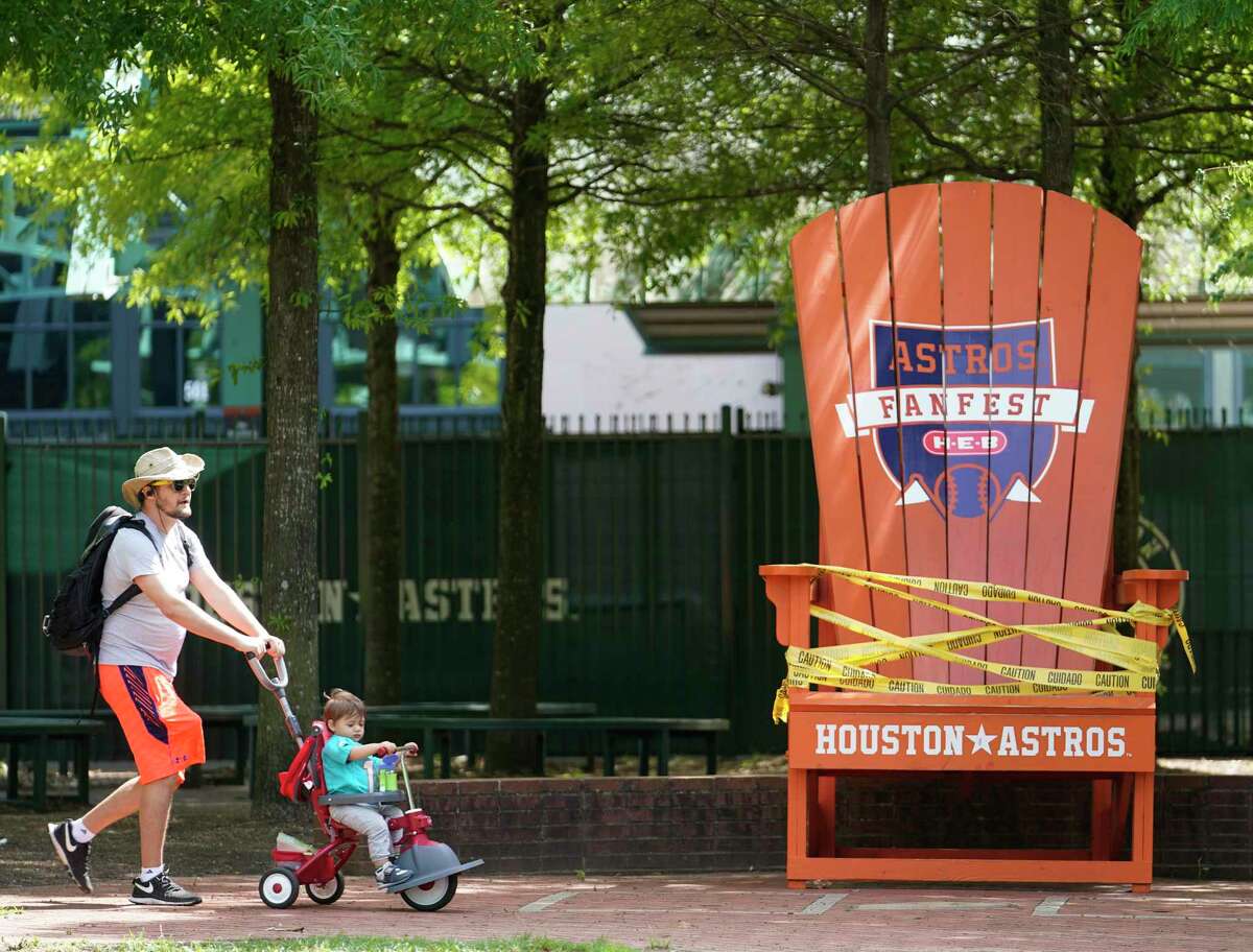 Daniel Estebanez pushes his 19-month-old son, Lucas Estebanez, by the cordoned off giant Houston Astros chair in the Plaza at Minute Maid Park Wednesday, April 29, 2020, in Houston. Major League Baseball delayed the start of the season amid the Covid-19 pandemic.