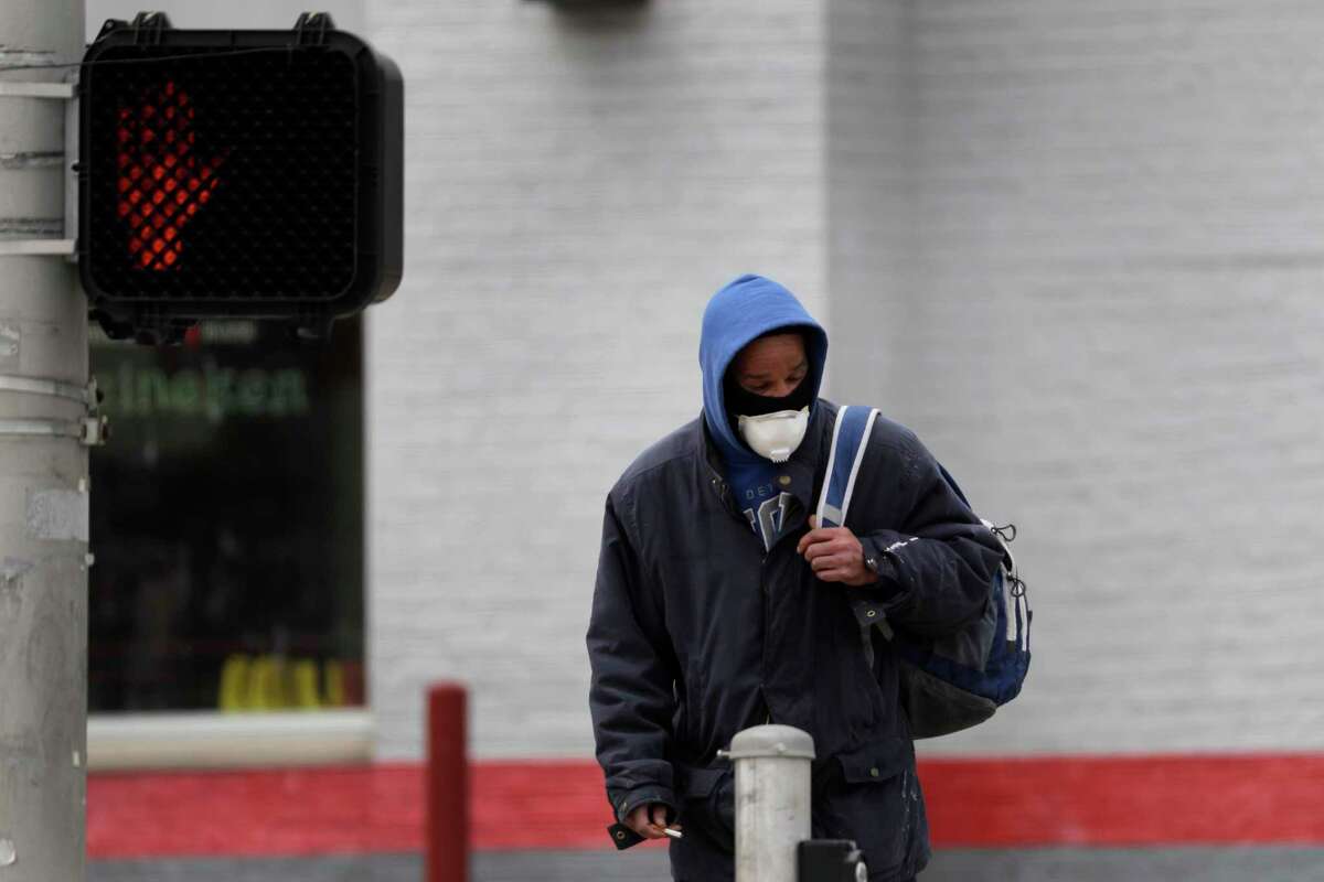A man wears a protective mask as he waits to cross a street Monday, April 13, 2020, in St. Louis where parts of the city have been hit much harder than others by the coronavirus outbreak. Of people who are known to have died from from COVID-19 in St. Louis, black people are dying at a much higher rate than other populations. (AP Photo/Jeff Roberson)