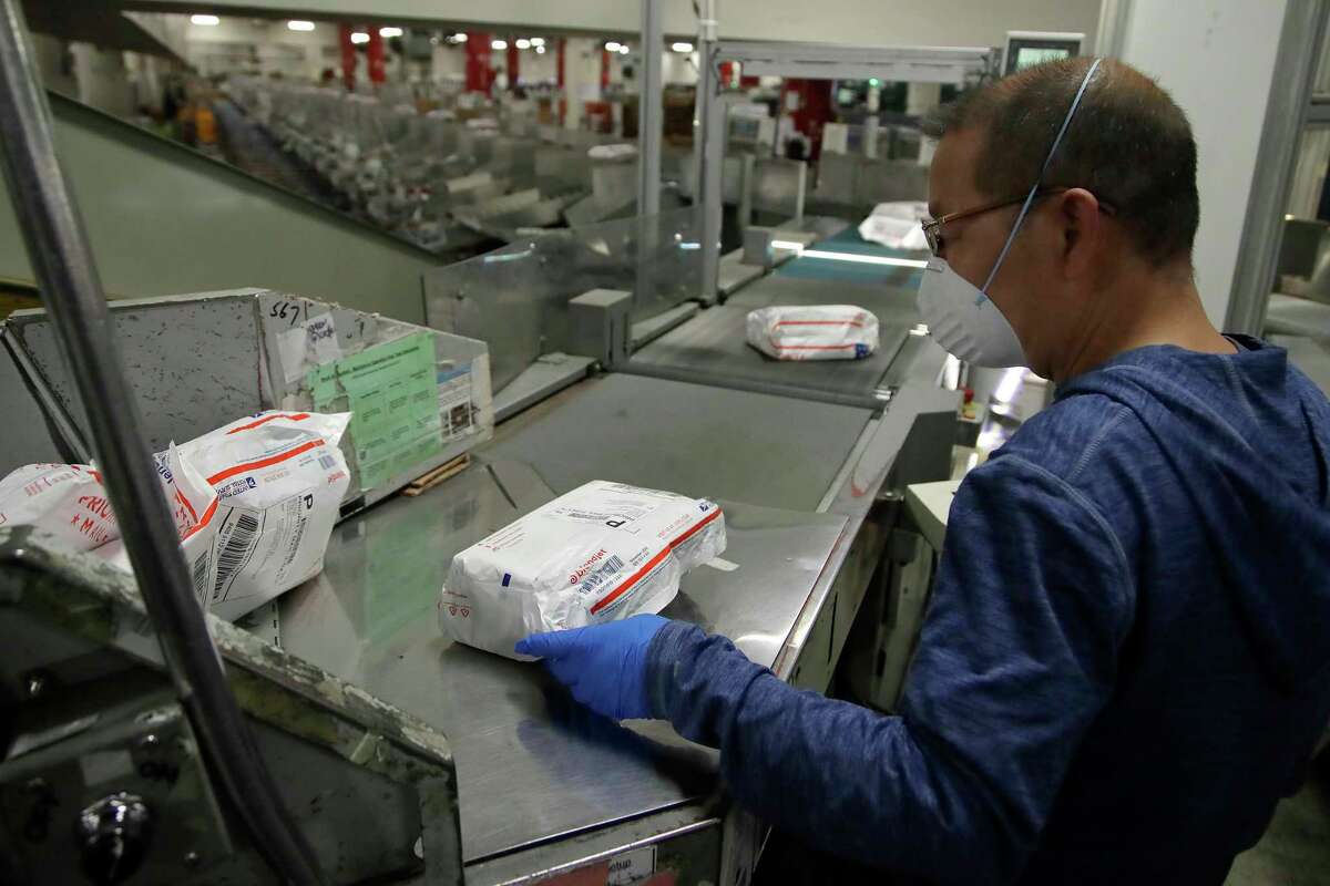 Postal worker Wing Yu wears a mask and gloves as he sorts mail at the United States Postal Service processing and distribution center on Thursday, April 30, 2020, in Oakland, Calif.