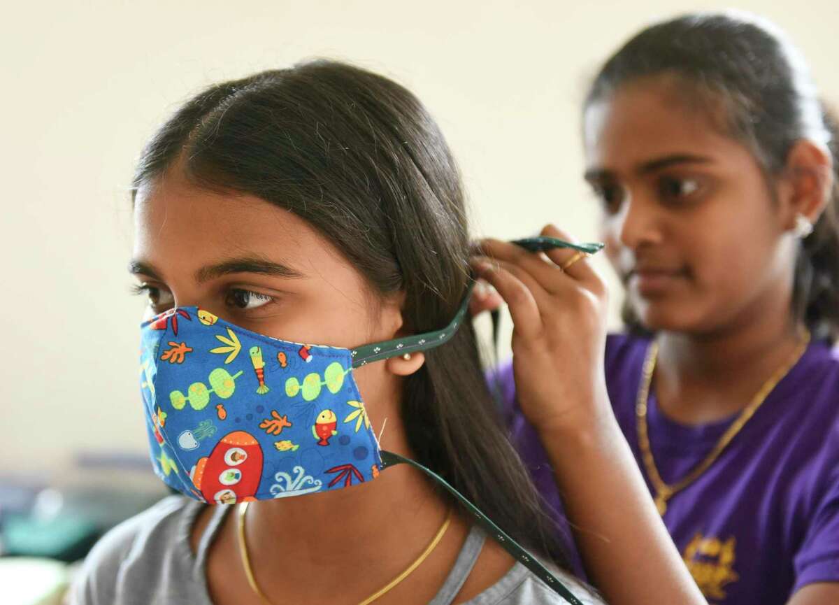 Dharana Alilaikannan, 14, ties a homemade face covering on her sister, Tanisha, 11, at their home in Stamford, Conn. Wednesday, April 29, 2020. The Stamford sisters Dharana and Tanisha Alilaikannan have been making masks with their mother, Tamilselvi, and a team of 20 volunteers to distribute to Stamford Hospital and Stamford Police Department, as well as some doctors, nurses and dentists in Greenwich.