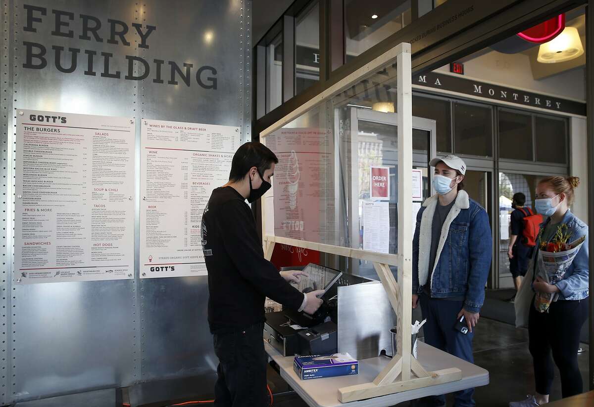 Angel Rivera (left) takes an order through a plexiglas barrier from Philip Bale and Weatherly Langsett at Gott's Roadside restaurant at the Ferry Building in San Francisco, Calif. on Saturday, May 2, 2020. Gott's Roadside restaurant has reopened its San Francisco location for takeout service using social distancing guidelines.