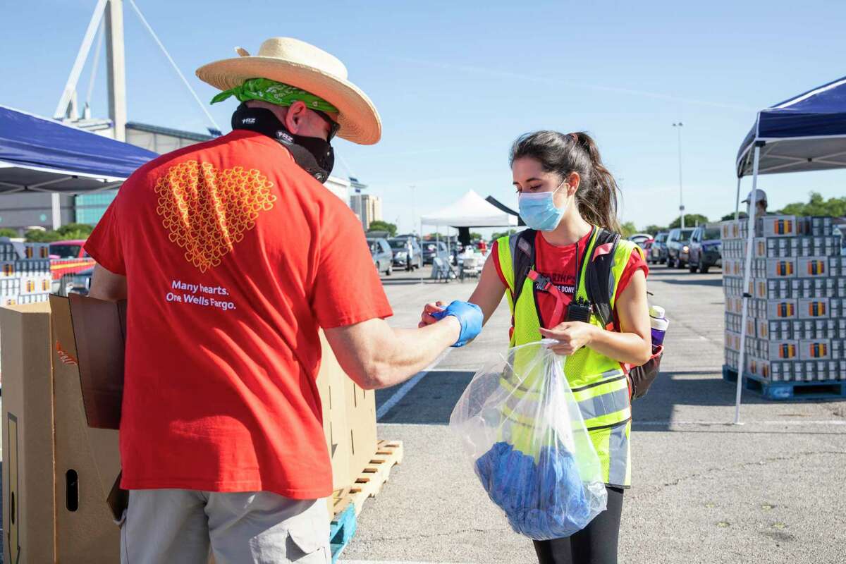 Brittany Jones, right, passes out latex gloves to volunteers during a food distribution event at the Alamodome, organized by the San Antonio Food Bank on Friday, May 1, 2020. Jones, a San Antonio native who graduated from Texas A&M at College Station, joined AmeriCorps to work with the San Antonio Food Bank where she has been organizing and distributing food to those in need during the coronavirus global pandemic.